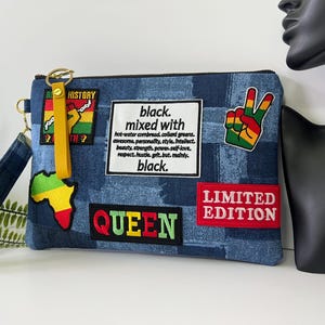 May include: A blue denim clutch bag with a wrist strap, featuring various patches including a map of Africa, a peace sign, and a white rectangular patch with the text black. mixed with hot-water cornbread, collard greens, and more.