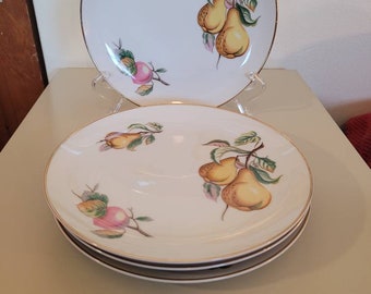 May include: White ceramic plates with a gold rim, featuring a hand-painted design of yellow pears and pink apples with green leaves. The plates are stacked, with one plate displayed on a clear stand.