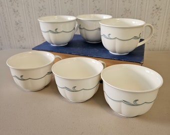 May include: Set of six white teacups with a blue and green wave design. The cups are arranged in two rows of three, with the top row slightly offset from the bottom row.