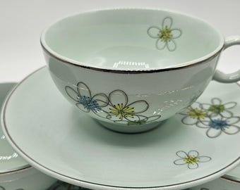 May include: A set of light green teacups and saucers with a floral design. The teacups have a handle and a dark rim. The floral design includes yellow, blue, and white flowers.