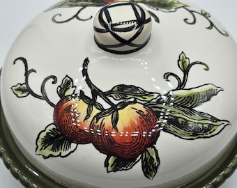 Puede incluir: Una mantequillera de cerámica con tapa en forma de cúpula color crema que presenta una ilustración pintada a mano de tomates rojos y vainas de guisantes verdes. La tapa tiene un pomo redondo con patrón de rejilla negro y base verde oliva.