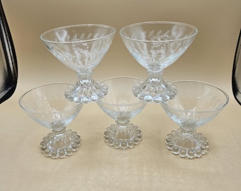 Puede incluir: Cinco copas de postre o cóctel de cristal transparente. Las copas tienen una base con diseño de cuentas y un cuenco acampanado. Dos copas están apiladas encima de otras tres. Los cuencos tienen un delicado diseño floral grabado.