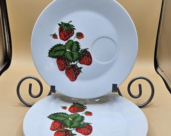 May include: Three white ceramic plates with a red strawberry design. The plates have a small indentation in the center, which is perfect for a cup or saucer.