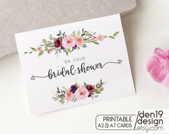 May include: White card with the text "On your bridal shower" in elegant script, adorned with floral arrangements in shades of pink, burgundy, and green. The card includes a small heart detail and the text "PRINTABLE A2 & A7 CARDS / den19 design .etsy.com".