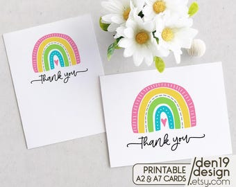 Puede incluir: Tarjetas de agradecimiento imprimibles con un diseño de arcoíris en colores rosa, amarillo, verde y azul. El arcoíris tiene un corazón en el centro y el texto "gracias" está escrito en cursiva negra.