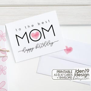 May include: A white greeting card with the text "to the best MOM happy birthday" in black. The word "MOM" has a pink watercolor heart in the center. A matching envelope is visible, along with a small graphic that says "PRINTABLE A2 & A7 CARDS + ENVELOPES / den19 design / etsy.com".