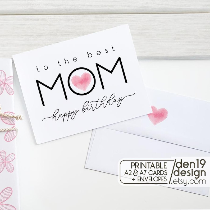 May include: A white greeting card with the text "to the best MOM happy birthday" in black. The word "MOM" has a pink watercolor heart in the center. A matching envelope is visible, along with a small graphic that says "PRINTABLE A2 & A7 CARDS + ENVELOPES / den19 design / etsy.com".