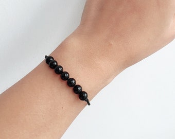 May include: A black beaded bracelet with a simple knot closure. The bracelet is made with round, black beads and a black string.