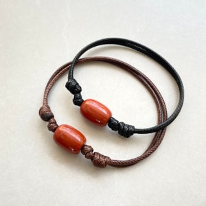 May include: Two bracelets with red stone beads and black and brown cords.