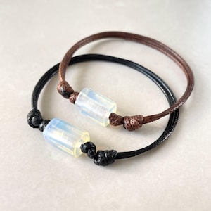 May include: Two bracelets with a white opal bead on each. One bracelet is brown cord and the other is black cord.