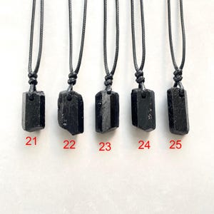 Peut inclure: Cinq pendentifs en cristal brut noir suspendus &agrave; des colliers en cordon noir. Chaque pendentif a une forme unique et est &eacute;tiquet&eacute; avec les chiffres rouges 21, 22, 23, 24 et 25, indiquant des pi&egrave;ces individuelles &agrave; choisir.