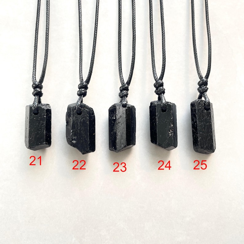 Peut inclure: Cinq pendentifs en cristal brut noir suspendus &agrave; des colliers en cordon noir. Chaque pendentif a une forme unique et est &eacute;tiquet&eacute; avec les chiffres rouges 21, 22, 23, 24 et 25, indiquant des pi&egrave;ces individuelles &agrave; choisir.