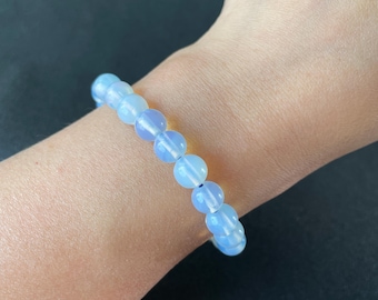 Könnte beinhalten: Ein Armband aus hellblauen Opalperlen. Das Armband befindet sich an einem Handgelenk.