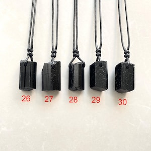 Peut inclure: Cinq pendentifs en cristal de tourmaline noire suspendus &agrave; des colliers en cordon noir. Chaque pierre brute a une forme unique et est suspendue par une boucle nou&eacute;e. Les pendentifs sont &eacute;tiquet&eacute;s avec les chiffres rouges 26, 27, 28, 29 et 30.