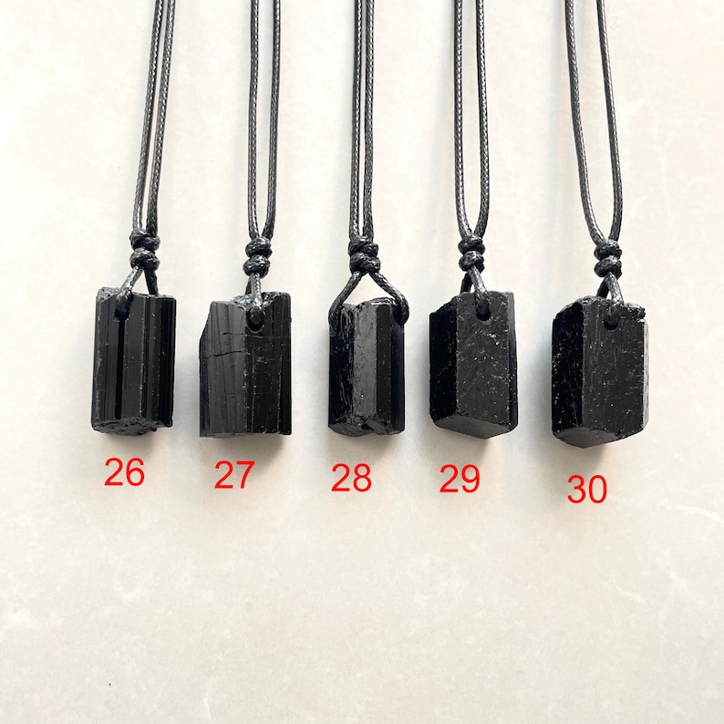 Peut inclure: Cinq pendentifs en cristal de tourmaline noire suspendus &agrave; des colliers en cordon noir. Chaque pierre brute a une forme unique et est suspendue par une boucle nou&eacute;e. Les pendentifs sont &eacute;tiquet&eacute;s avec les chiffres rouges 26, 27, 28, 29 et 30.
