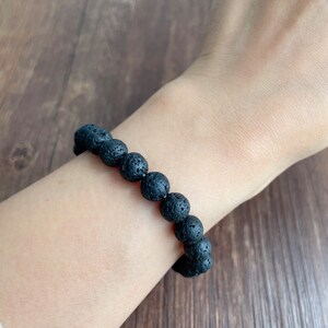 May include: A black lava rock beaded bracelet. The bracelet is made of round, black beads with a rough, textured surface.