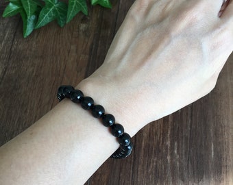 May include: A black beaded bracelet with round beads on a person's wrist.