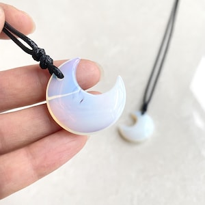 May include: A crescent moon pendant necklace made of iridescent opal with a black cord. The pendant is about 2 inches long.
