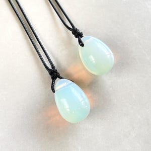 May include: Two teardrop-shaped opal pendants on black cords. The opals are a milky white color with a slight iridescent sheen.