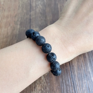 May include: A black lava rock beaded bracelet. The bracelet is made of round, black beads with a rough, textured surface.
