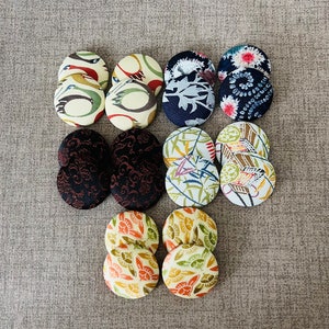 May include: Assortment of 12 round fabric buttons with various colorful floral and geometric patterns. The buttons are arranged in three rows of four.