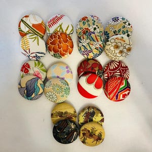 Op de afbeelding: Assortiment van 14 ronde stoffen knopen met verschillende Japanse geïnspireerde patronen, waaronder bloemen, geometrische en traditionele ontwerpen. De knopen zijn in tinten rood, blauw, groen, geel en wit.