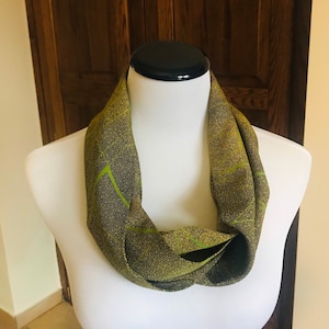 Könnte beinhalten: Ein grüner und goldener Infinity-Schal mit geometrischem Muster. Der Schal ist aus einem weichen, schimmernden Stoff.