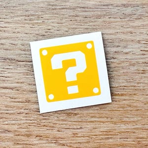 May include: A yellow square with a white question mark inside. The square has a white border and four white dots on the corners.