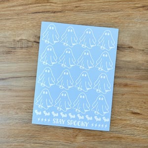 May include: A light blue rectangular sheet featuring a repeating pattern of sixteen white ghost illustrations arranged in four rows. Below the ghosts is a row of small white bat silhouettes, the text STAY SPOOKY, and several small white lightning bolts.