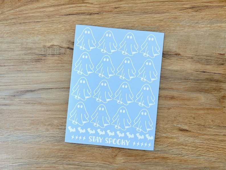 May include: A light blue rectangular sheet featuring a repeating pattern of sixteen white ghost illustrations arranged in four rows. Below the ghosts is a row of small white bat silhouettes, the text STAY SPOOKY, and several small white lightning bolts.