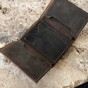 May include: A brown leather wallet with multiple card slots and a billfold. The wallet is open and the interior is visible.