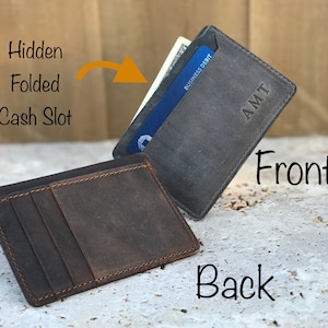 May include: A brown leather wallet with a hidden cash slot and a separate card slot. The front of the wallet is grey and has the initials "AMT" embossed on it.