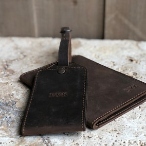 Puede incluir: Un conjunto de accesorios de viaje de cuero marr&oacute;n oscuro, que incluye una etiqueta de equipaje con correa y una cartera. Ambos art&iacute;culos est&aacute;n grabados con las iniciales "EYK". El cuero tiene un aspecto texturizado y los art&iacute;culos est&aacute;n cosidos con un hilo m&aacute;s claro.