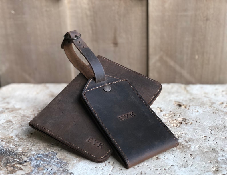 May include: A set of brown leather travel accessories, including a wallet and luggage tag. The wallet and tag are embossed with the initials "EYK". The luggage tag has a strap with a buckle.