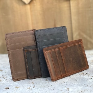 May include: Three leather wallets in brown, dark brown, and blue. The wallets are made of distressed leather and have multiple card slots.