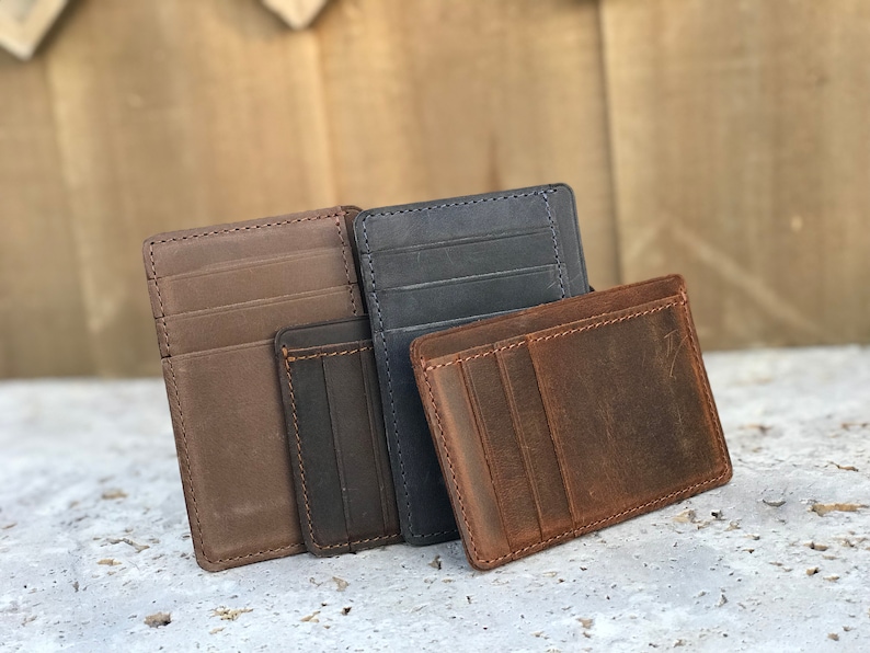 May include: Three leather wallets in brown, dark brown, and blue. The wallets are made of distressed leather and have multiple card slots.