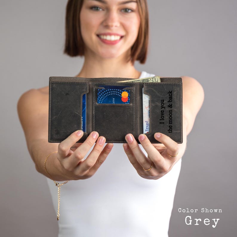 May include: A grey leather wallet with a personalized inscription that reads "I love you the moon & back". The wallet is open to show the interior card slots and cash compartment.