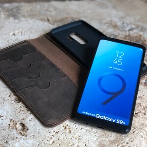K&ouml;nnte beinhalten: Ein braunes Leder-Telefonetui mit Steckpl&auml;tzen f&uuml;r Karten und ein schwarzes Telefonetui f&uuml;r ein Samsung Galaxy S9+ Telefon. Der Telefonbildschirm zeigt die Uhrzeit 12:45 und das Datum Sonntag, 25. Februar.