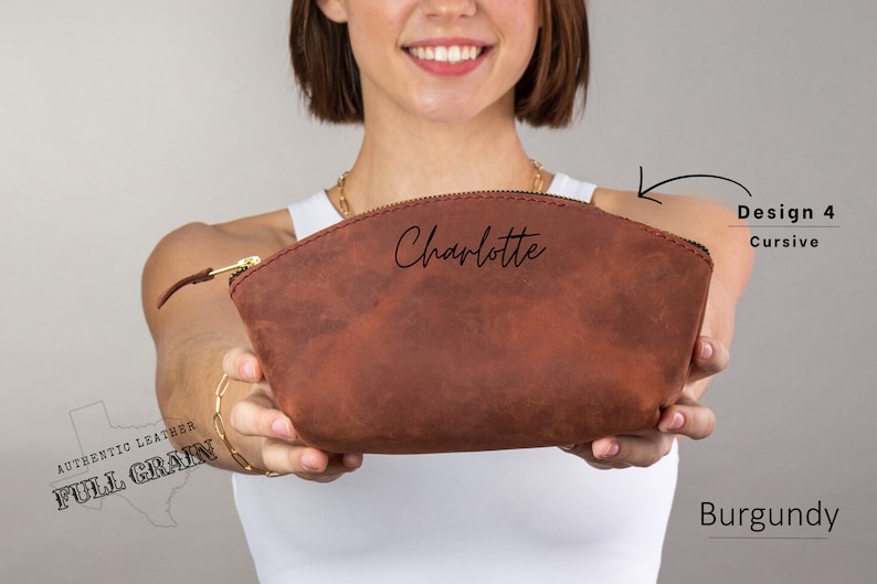 May include: Burgundy leather makeup bag with a zipper closure and the name "Charlotte" written in cursive on the front. The bag is made of full grain leather.