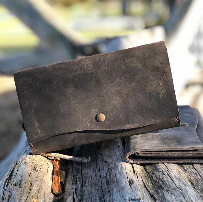May include: Two brown leather wallets with a distressed finish. The top wallet has a brass button closure.
