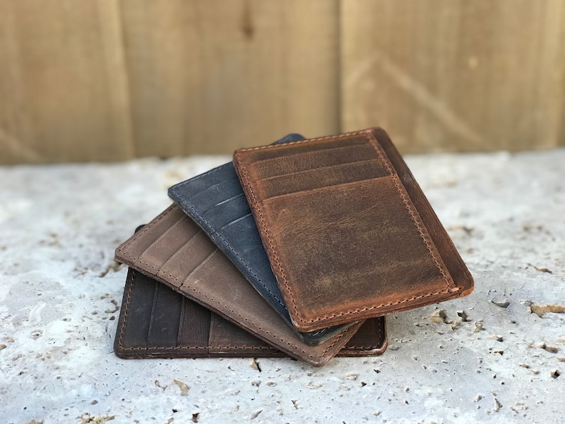 May include: Four leather card holders in different colours: brown, tan, grey, and dark blue. The card holders are stacked on top of each other.