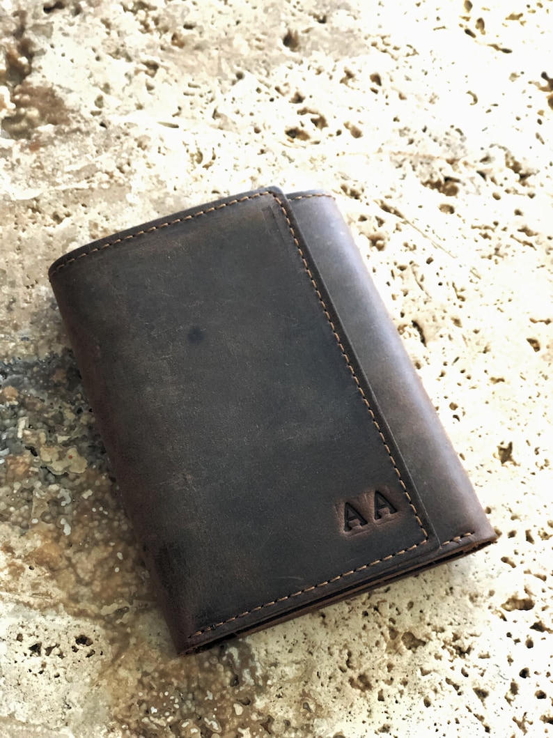 May include: A brown leather trifold wallet with the initials "AA" embossed on the front.