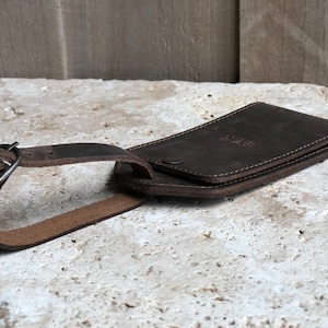 Puede incluir: Una etiqueta de equipaje de cuero marr&oacute;n oscuro con correa y hebilla. La etiqueta es rectangular con esquinas redondeadas y las iniciales "SVR" grabadas en la parte delantera. La etiqueta est&aacute; dise&ntilde;ada para guardar una tarjeta.