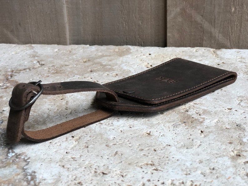Puede incluir: Una etiqueta de equipaje de cuero marr&oacute;n oscuro con correa y hebilla. La etiqueta es rectangular con esquinas redondeadas y las iniciales "SVR" grabadas en la parte delantera. La etiqueta est&aacute; dise&ntilde;ada para guardar una tarjeta.