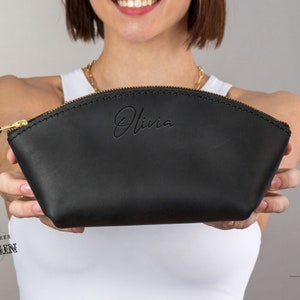 May include: Black leather cosmetic bag with a gold zipper and the name "Olivia" embossed on the front. The bag is made of full grain leather.