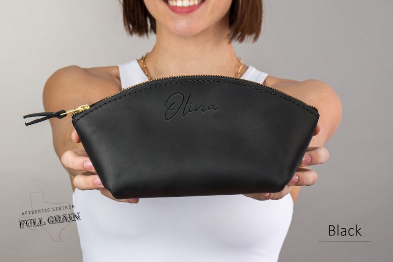 May include: Black leather cosmetic bag with a gold zipper and the name "Olivia" embossed on the front. The bag is made of full grain leather.