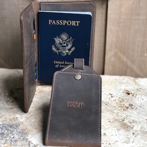 Puede incluir: Un portapasaporte de cuero marr&oacute;n con un pasaporte azul en su interior. Una etiqueta de equipaje a juego con las iniciales "EYK" est&aacute; al frente. El portapasaporte tiene ranuras para tarjetas. Los art&iacute;culos est&aacute;n sobre una superficie texturizada.