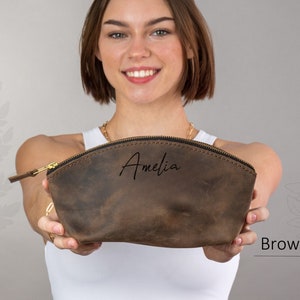 May include: A brown leather makeup bag with a zipper closure. The bag is personalized with the name "Amelia" in black script.