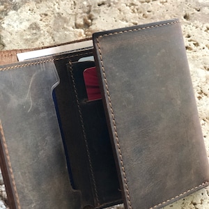 May include: A brown leather wallet with multiple card slots and a billfold. The wallet is open and shows the interior lining.