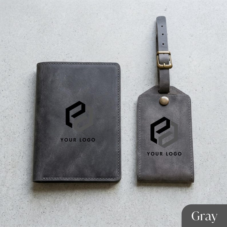 May include: Gray leather passport holder and luggage tag set. Both items feature a black logo and the text "YOUR LOGO". The luggage tag has a buckle and strap. The set is designed for travel.